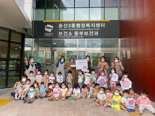 민락사랑어린이집 아이들과 선생님들이 송산3동 행정복지센터 1층 현관 앞에서 기념촬영을 하고 있다.
